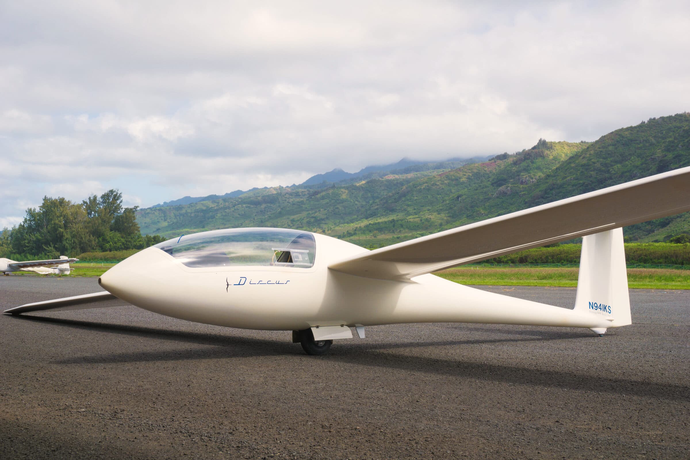 Sleek white Discus sailplane parked on the tarmac under a blue Hawaiian sky